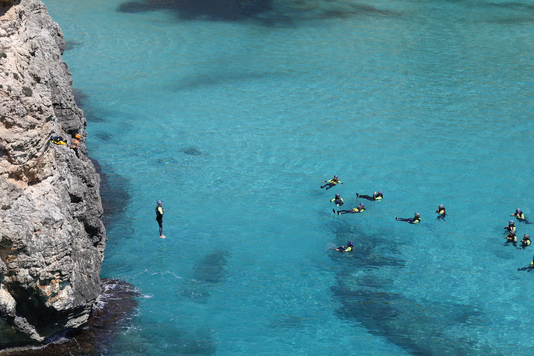 A group of people floating in clear turquoise water beside a rocky cliff