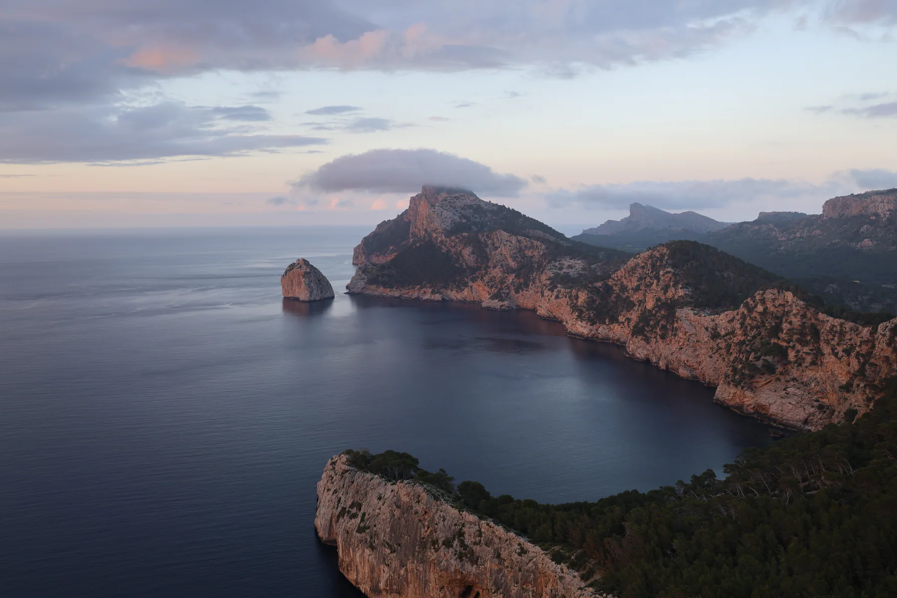 Rocky Mallorca coastline extending into a calm sea beneath low clouds