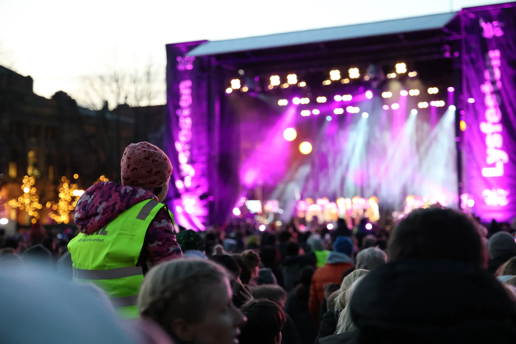 A child in a reflective vest watching a brightly lit outdoor concert