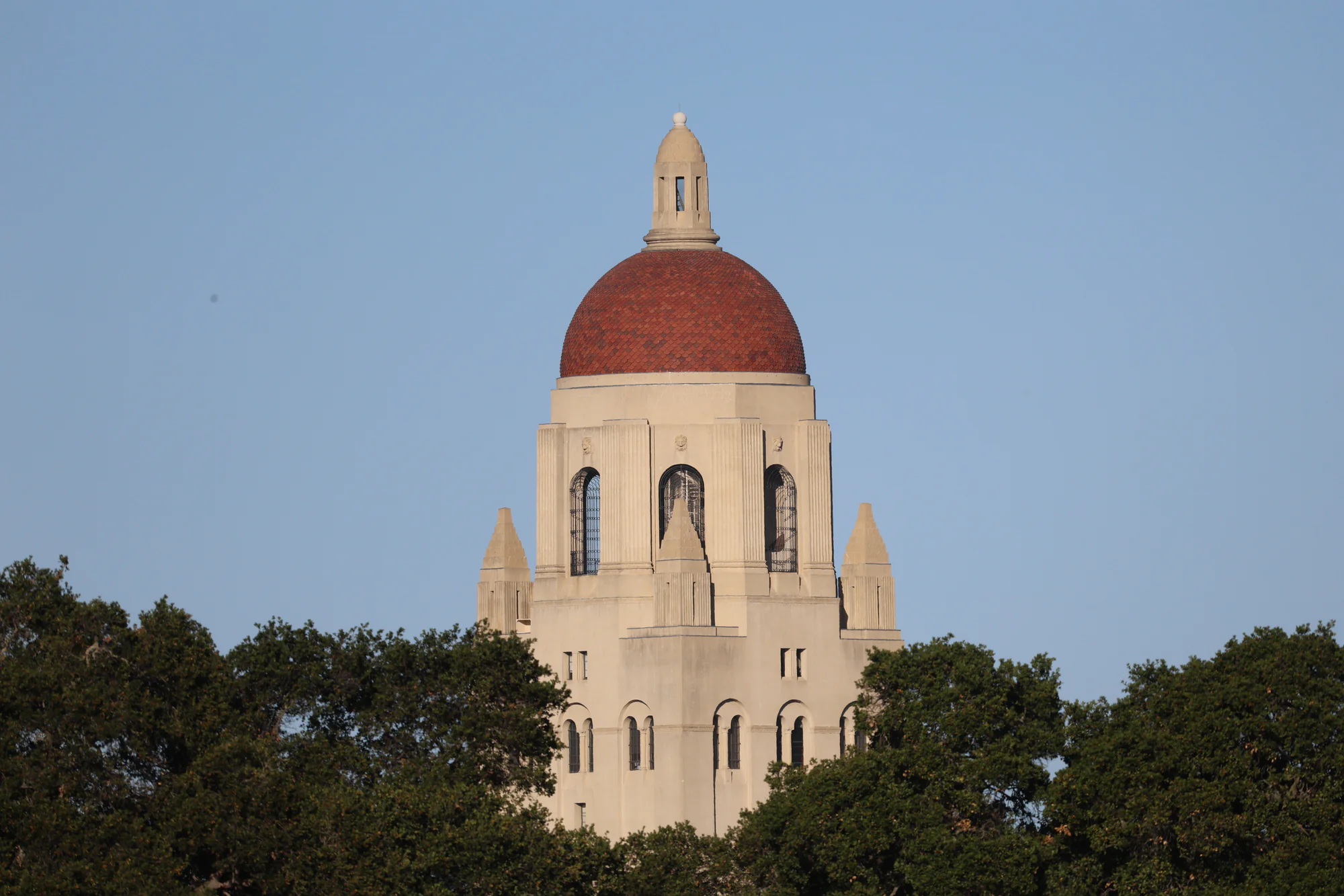 Stanford’s Hoover Tower with its red-tiled dome rising above green trees against a blue sky.