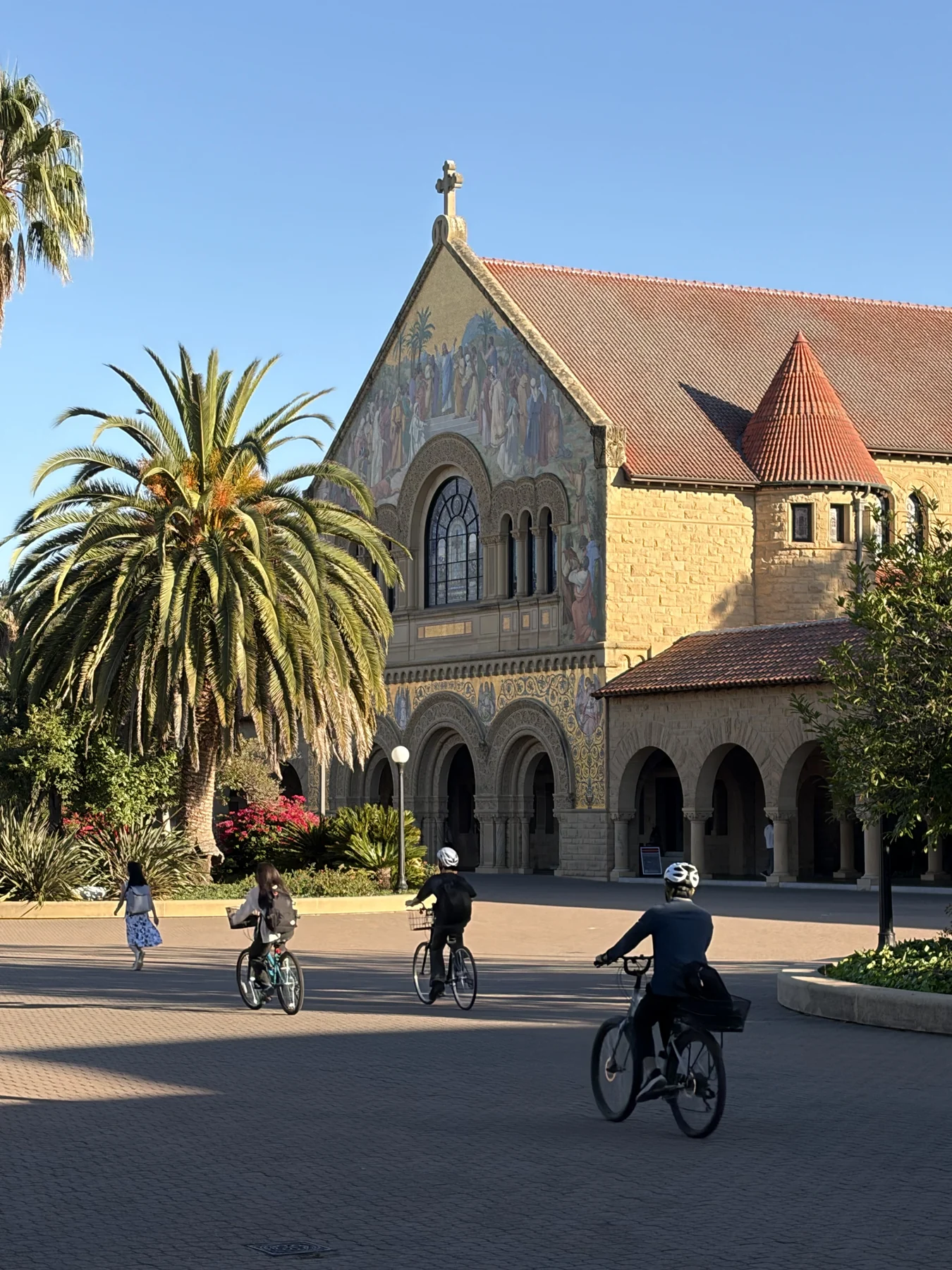 Stanford Memorial Church and palm trees, with cyclists crossing the Main Quad.